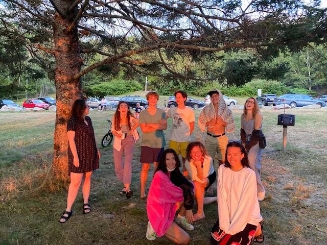 The crew gathered under a pine tree at golden hour.