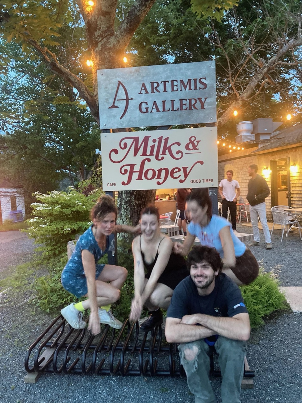 Four of the crew posing at the Milk & Honey sign at dusk, under string lights.