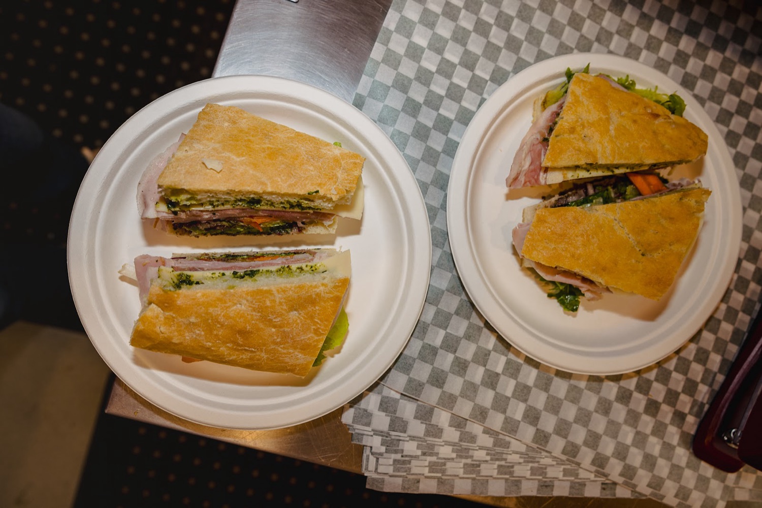Two focaccia sandwiches, halved, on paper plates on the café’s checkerboard counter.
